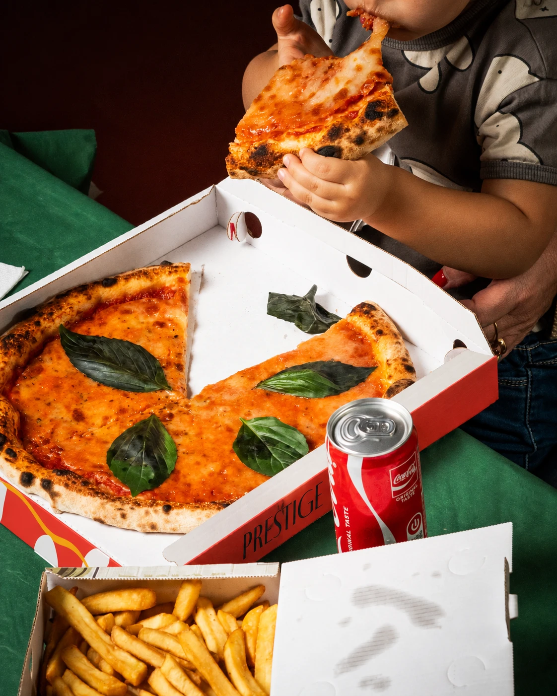 Un bambino mangia una fetta di margherita accanto al cartone Prestige